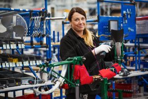 Female skilled factory worker assembling a bicycle in a factory working on the frame and wheels.